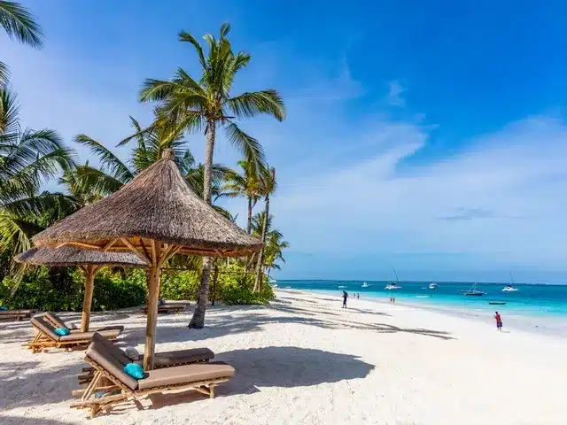 Paillote d'ombrage et transat sur une plage de sable blanc, lagon bleu turquoise