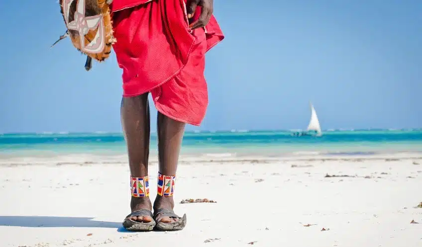 Tenue traditionnelle d’Afrique de l’Est sur une plage tropicale, lagon et boutre en arrière-plan